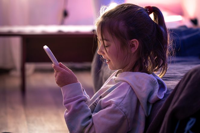 
 Portrait of a little girl with a smartphone in her hands in the interior of the room, the concept of gadget addiction.